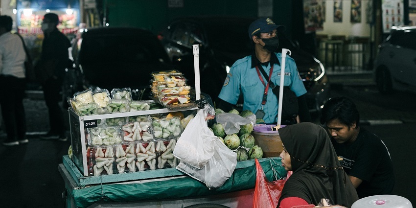 A street vendor in the market at night selling tropical fruits with cars parked , displaying Mauritius nightlife.
